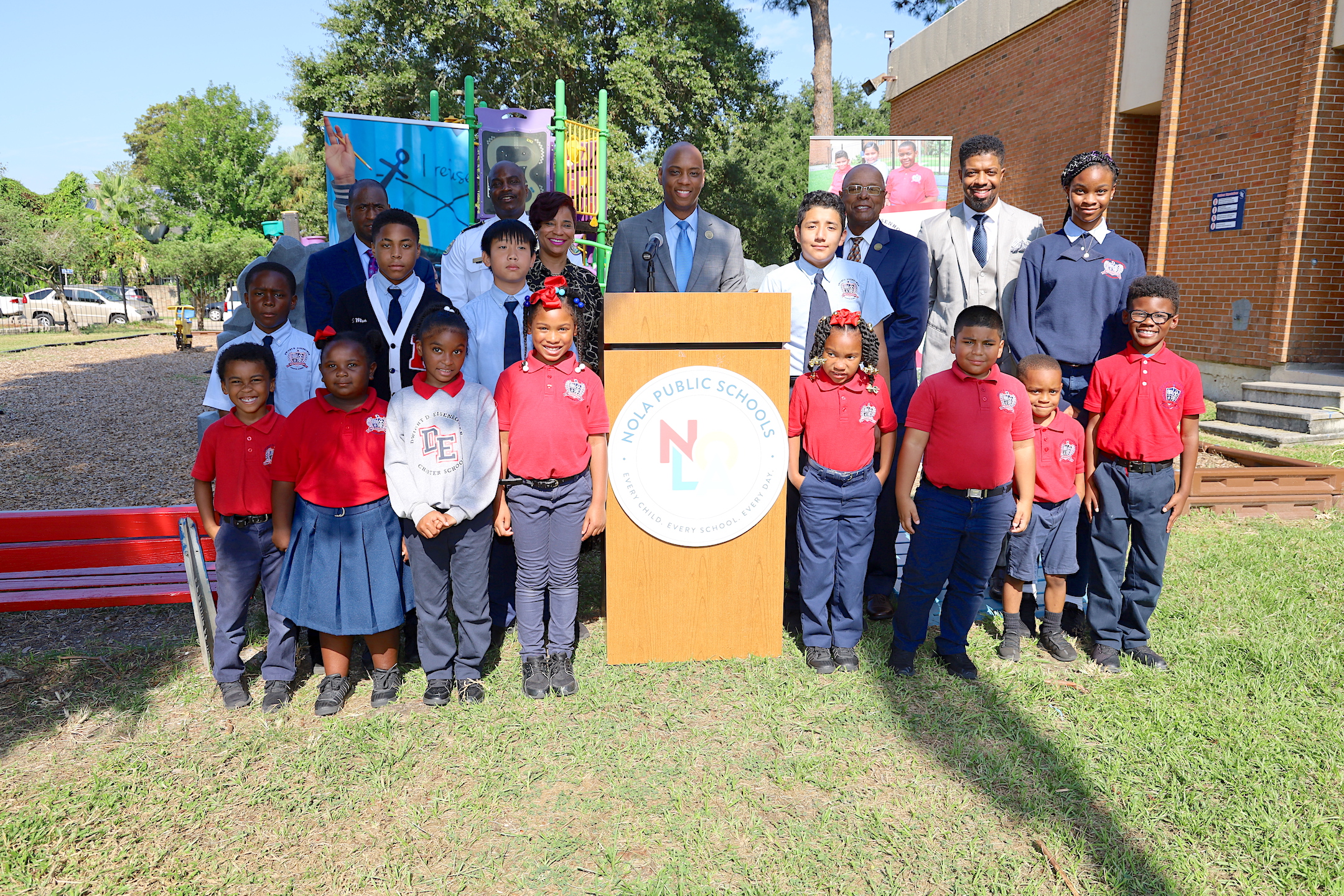 Superintendent Dr. Henderson Lewis, Jr. poses with staff and students behind a podium outside